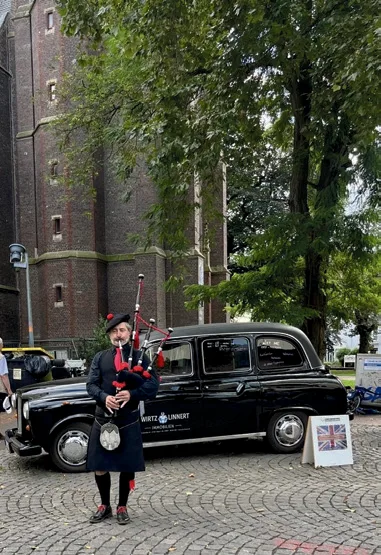 Ein Dudelsackspieler steht neben einem schwarzen englischen Taxi.