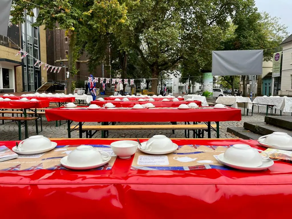 Eine lange rote Tafel ist mit weißen Tassen, Untertassen und Teekannen eingedeckt.